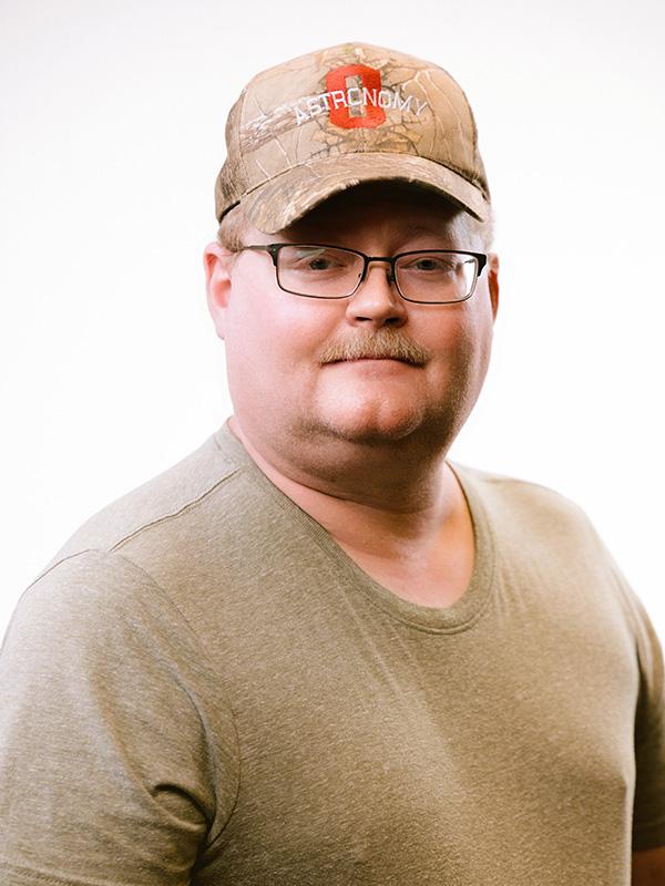 A man with a mustache wearing glasses, a brown t-shirt and an OSU ballcap