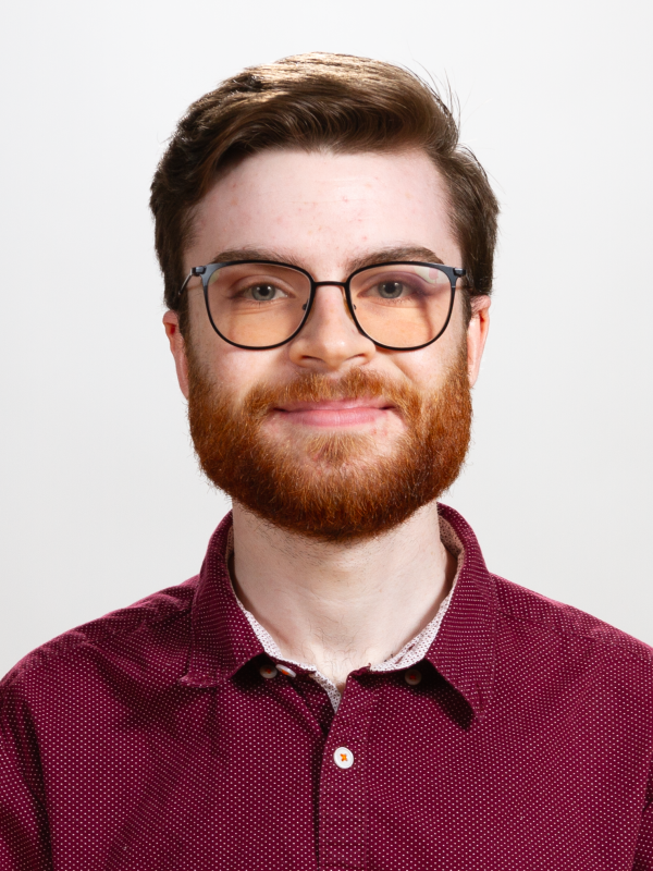 A bearded man wearing glasses and a magenta shirt