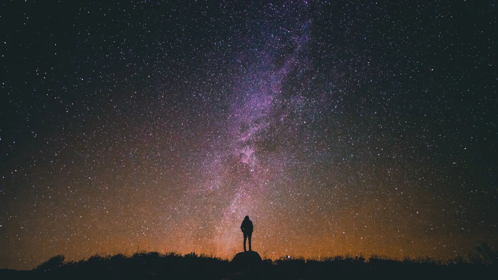 Man standing in front of the Milky Way at night. Credit: Greg Rakozy on Unsplash