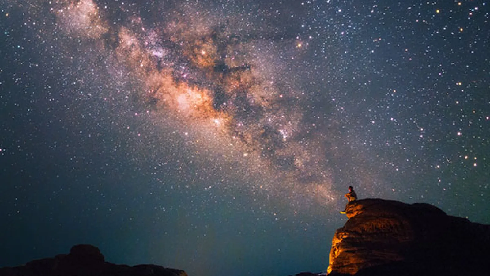 Milky Way Galaxy with Man sitting on cliff in foreground