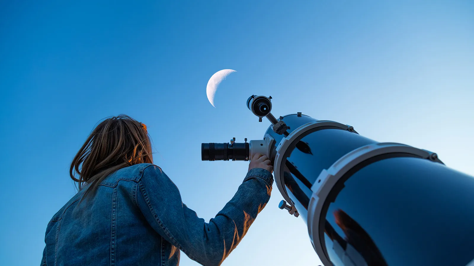 Woman looking at the moon next to a telescope