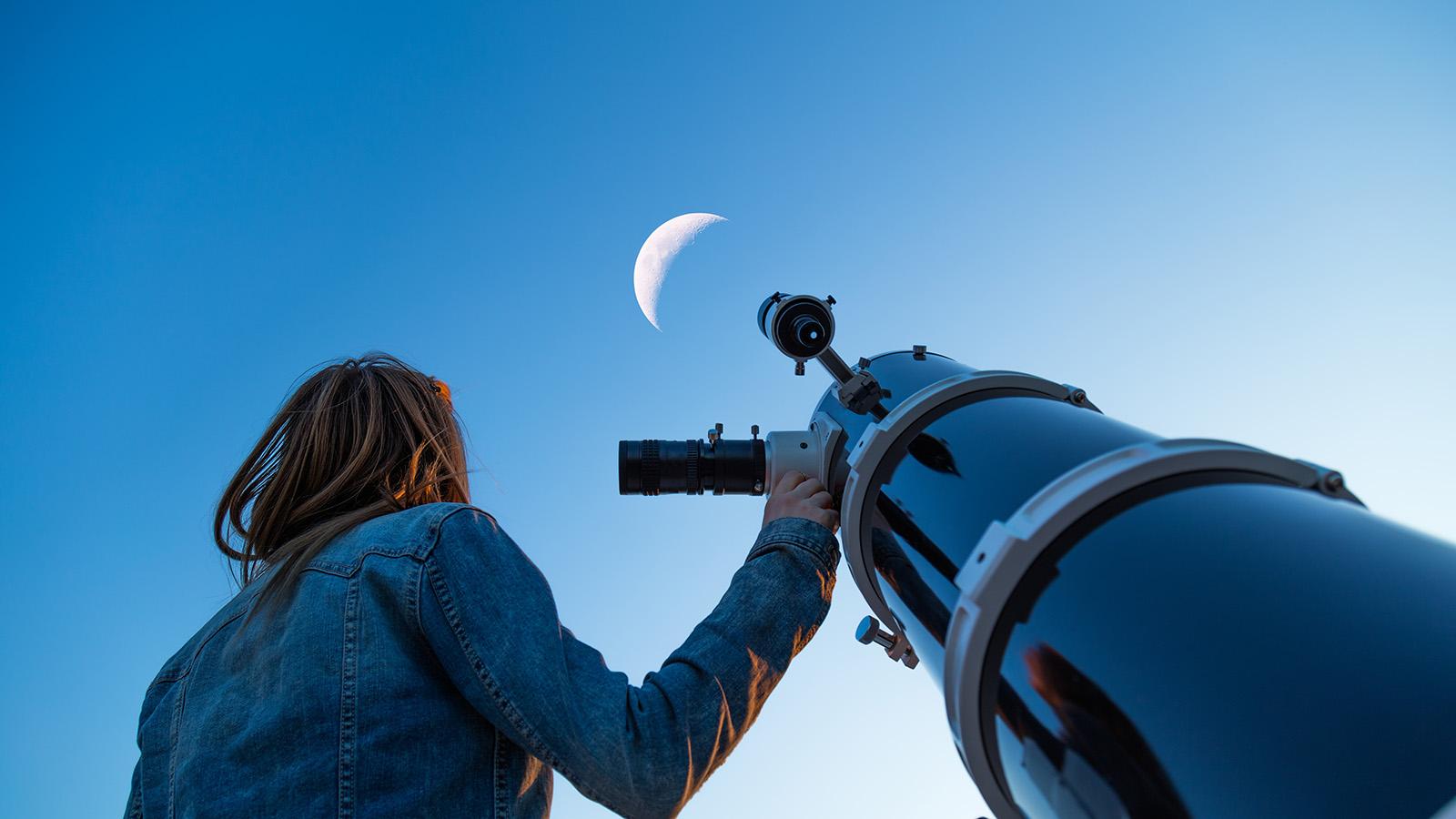 Woman looking at the moon next to a telescope