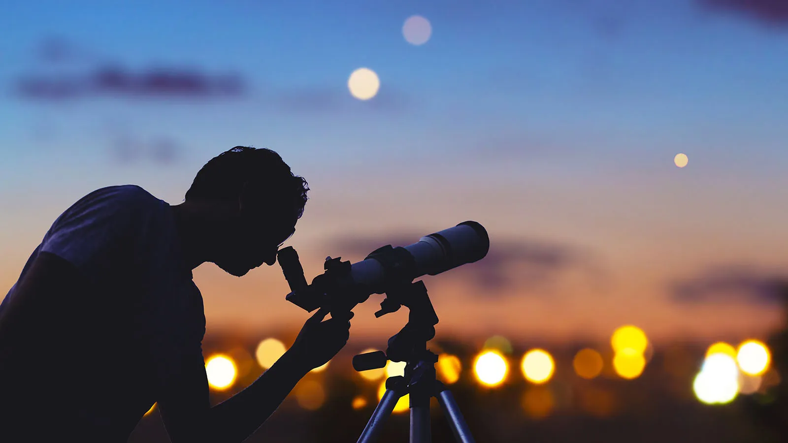 An astronomer using a small telescope at dusk