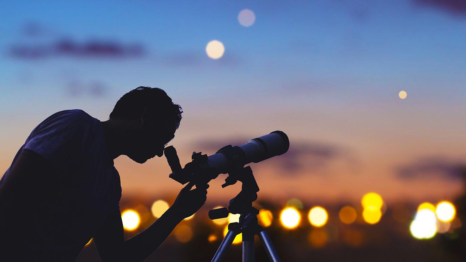 An astronomer using a small telescope at dusk