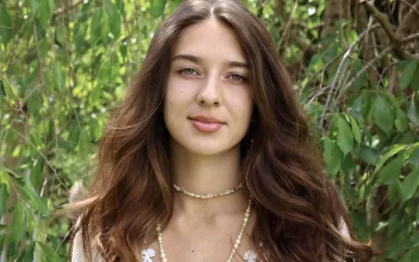 A woman with long brown hair wearing a thin chain necklace