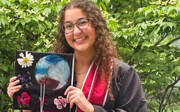 A smiling woman with long hair and glasses wearing academic robes
