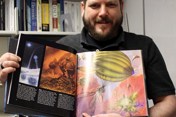 Photo of Professor Scott Guadi holding the book that inspired his interest in astronomy.