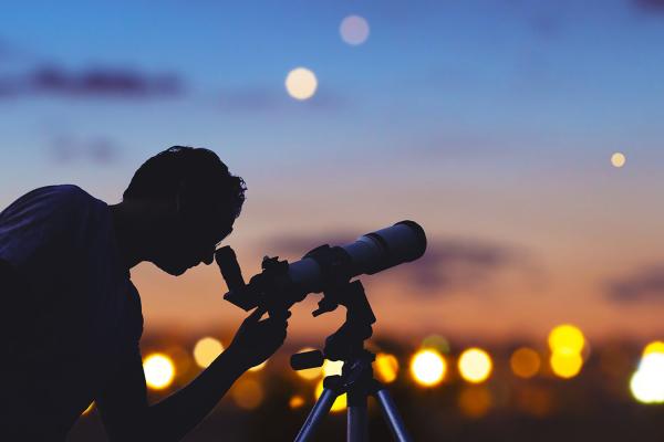 An astronomer using a small telescope at dusk