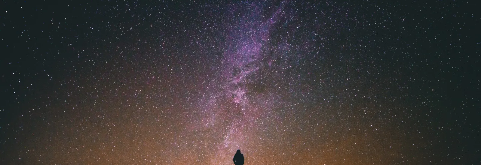 Man standing in front of the Milky Way at night. Credit: Greg Rakozy on Unsplash