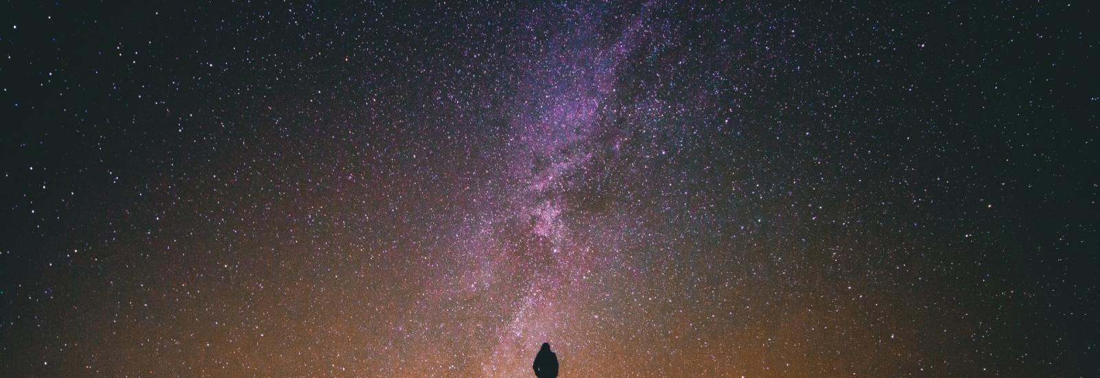 Man standing in front of the Milky Way at night. Credit: Greg Rakozy on Unsplash