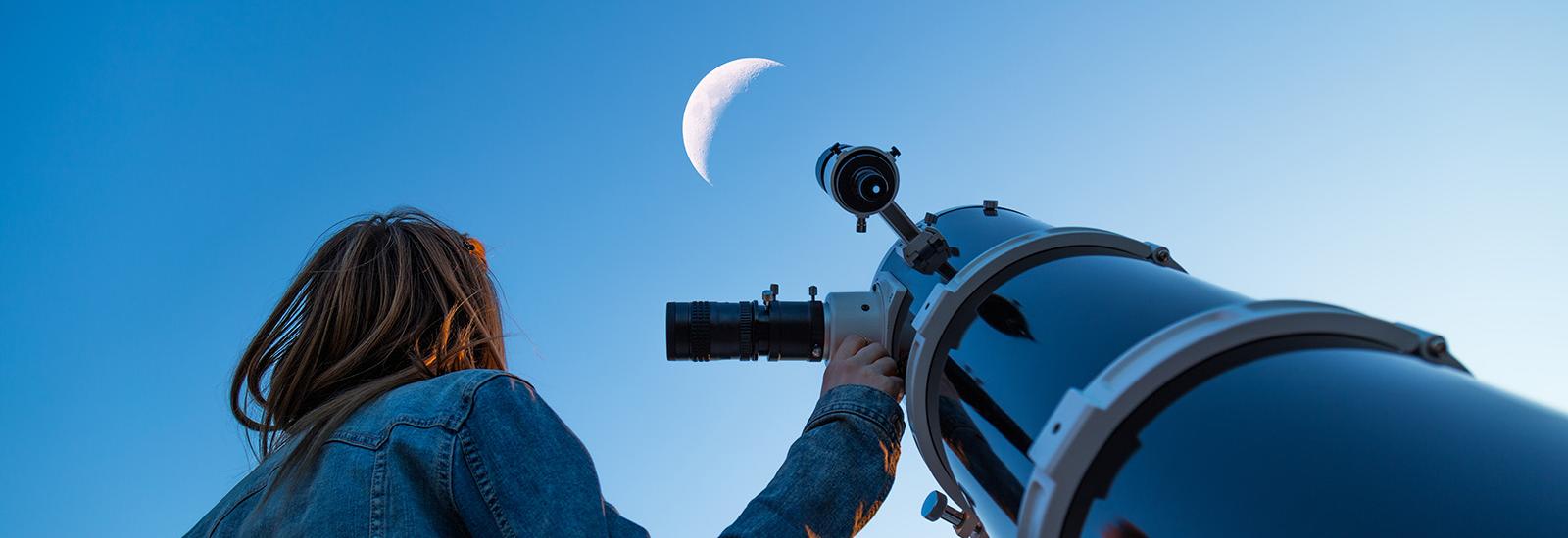 Woman looking at the moon next to a telescope